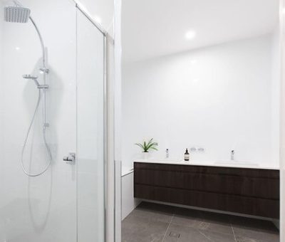 Modern bathroom with glass shower enclosure, rainfall showerhead, and floating dark wood vanity. 
