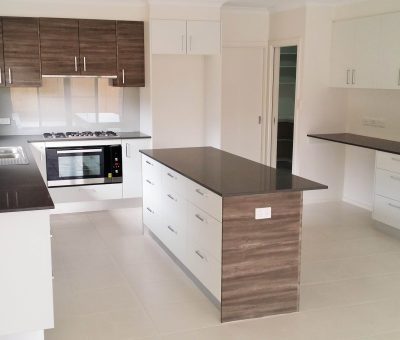Modern kitchen with sleek brown and white cabinetry, a central island with dark countertops, stainless steel appliances, and ample natural light.