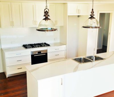 Modern kitchen with white cabinets, marble island, and stainless steel sink. Features pendant lights, gas stove, and wooden floors, evoking a bright, elegant feel.