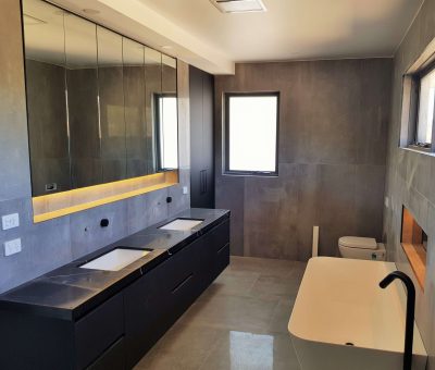 Contemporary bathroom with double vanity, mirrored cabinets, freestanding bathtub, and gray tiled walls.