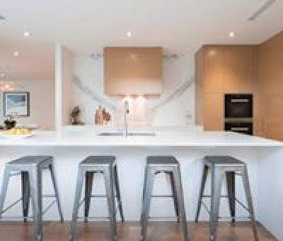 “Contemporary kitchen featuring a sleek white island with bar seating and warm timber finishes.”