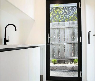 Minimalist white kitchen with black fixtures and a sleek black door leading to an outdoor area. The space is bright and modern, exuding simplicity.