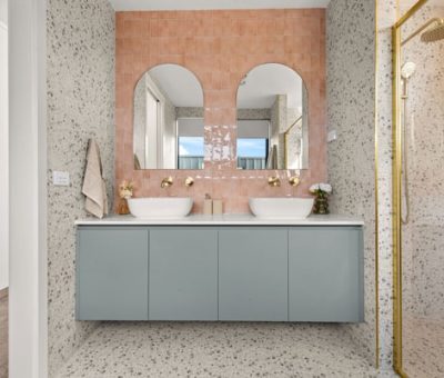 “Stylish bathroom design with terrazzo finishes, pink feature tiles, and twin sinks with arched mirrors.”