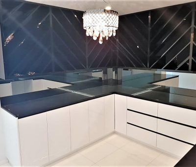 Sleek modern kitchen with white cabinets, black countertops, and a mirrored backsplash. A crystal chandelier adds elegance to the bright space.