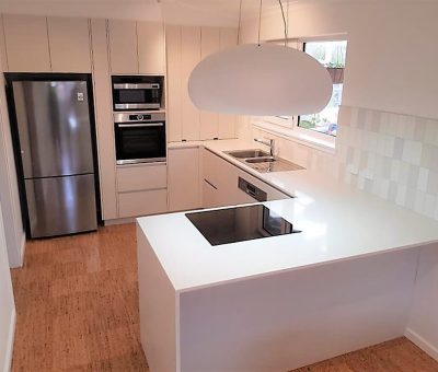 Modern kitchen with white cabinetry, stainless steel appliances, and wood flooring. An island with a stovetop and an oval pendant light adds elegance.