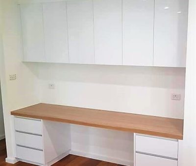 Modern home office setup with a wooden desk, white cabinets above, and drawers on either side. The clean, minimalist design conveys a tidy workspace.