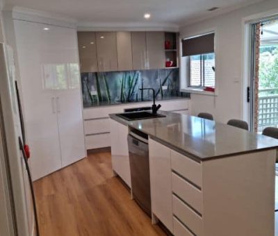 “Modern renovated kitchen featuring sleek white cabinetry, a functional island, and a vibrant glass backsplash.”