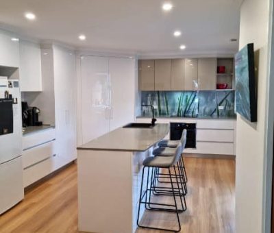 “Open and modern kitchen design with a sleek island, bar seating, and a bold glass backsplash feature.”