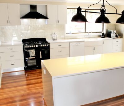 Modern kitchen with wooden floors, white cabinets, black stove and oven, large island, and industrial-style pendant lights. Bright and inviting.