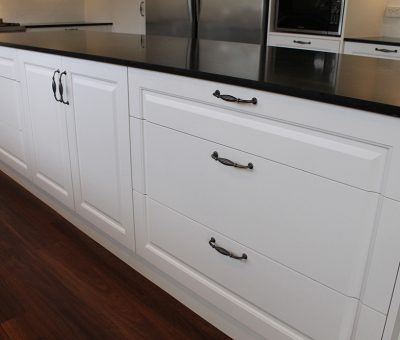 “Detail view of a classic white kitchen island with elegant black benchtop and hardware.”
