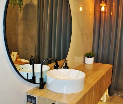 Modern bathroom with floating wood vanity, round basin sink, and large circular mirror with accent lighting.