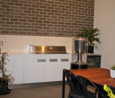 “Stylish alfresco kitchen with BBQ, sink, and dining area set against a brick feature wall.”