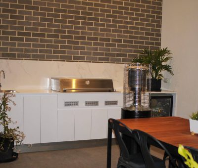 Stylish alfresco kitchen with BBQ, sink, and dining area set against a brick feature wall.