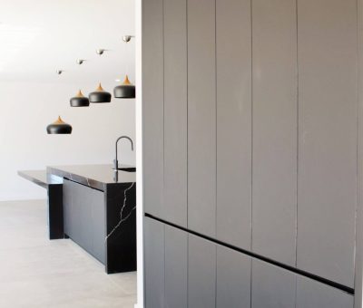 Minimalist kitchen with dark cabinets, black marble island, and modern pendant lights. Bright space with sleek, modern design and neutral tones.