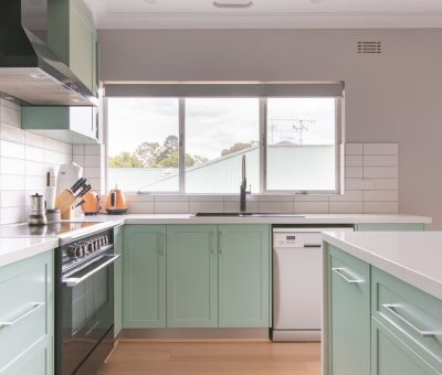A modern kitchen with mint green cabinets, white countertops, and stainless steel appliances. Large window with light, creating a bright, airy atmosphere.