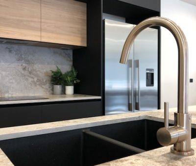 Modern kitchen with sleek black cabinetry and a stainless steel refrigerator. A shiny silver faucet is mounted on a light granite countertop.