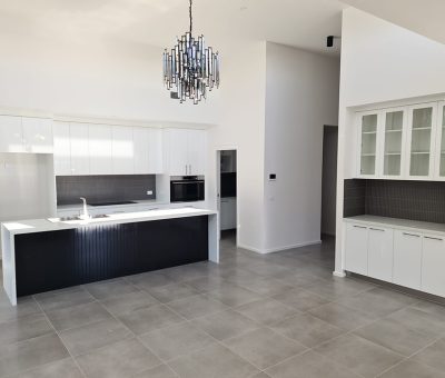 “Bright open kitchen featuring a black island, white cabinetry, and elegant chandelier.”