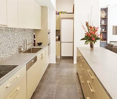 Modern kitchen with sleek beige cabinets, a patterned tile backsplash, and stainless steel appliances. A flower vase on the island adds warmth.