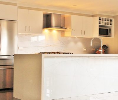Modern kitchen with stainless steel appliances, including a fridge and stovetop. White cabinets, sleek countertops, and under-cabinet lighting create a bright, clean atmosphere.