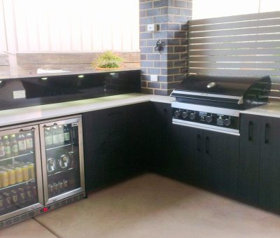 Outdoor kitchen with a sleek modern design; features a stainless steel grill, double-door fridge stocked with beverages, and ample counter space.