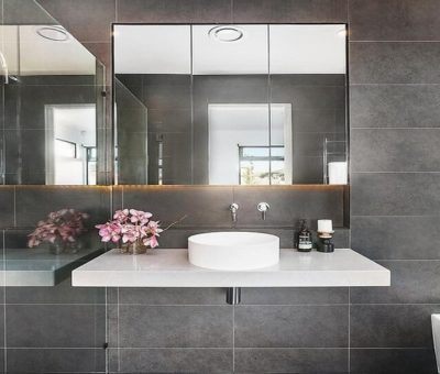 Modern bathroom with dark tiled walls, floating vanity, round basin, and mirrored cabinets.