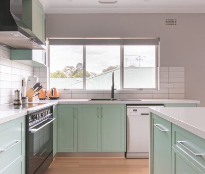 “Bright renovated kitchen with mint green cabinetry and modern stainless steel appliances.”
