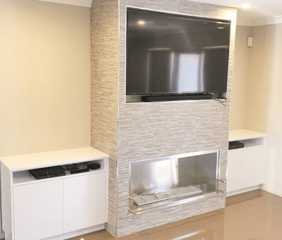 Modern living room setup with a large TV mounted on a stone-textured wall above a sleek, minimalist fireplace. White cabinets flank each side. Cozy and elegant.