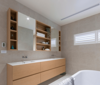 Minimalist bathroom with floating wood vanity, wall-mounted taps, and built-in shelving beside mirrors.