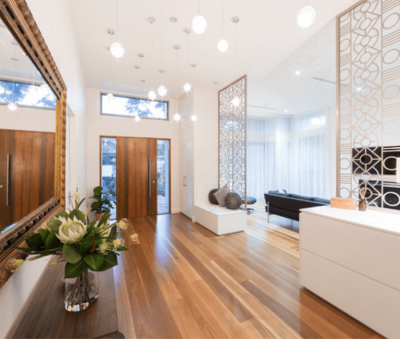 Modern interior with wooden floors, a large ornate mirror, and decorative screens. A vase with flowers and soft pendant lighting create an elegant, warm ambiance.