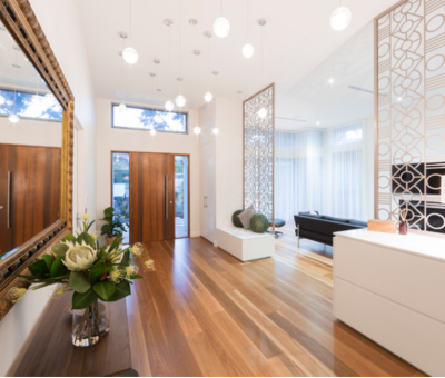 Modern interior with wooden floors, a large ornate mirror, and decorative screens. A vase with flowers and soft pendant lighting create an elegant, warm ambiance.