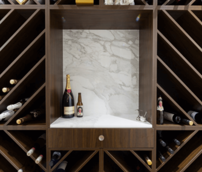 Wooden wine rack with diagonal shelves, filled with various bottles. A central alcove displays one champagne and one beer bottle on a marble backdrop.