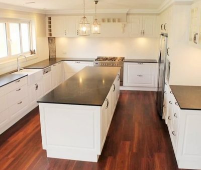 Spacious kitchen with white cabinets, black countertops, and a central island. Hardwood floors and pendant lights create a warm, modern ambiance.