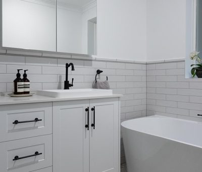 Bright, modern bathroom with white cabinetry, black fixtures, and freestanding tub. Gray patterned tile floor and arched mirror create a clean, serene ambiance.