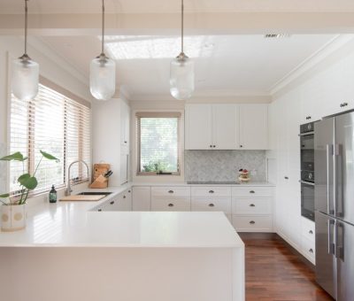 “Fresh white kitchen with pendant lights, stainless steel appliances, and warm timber accents.”