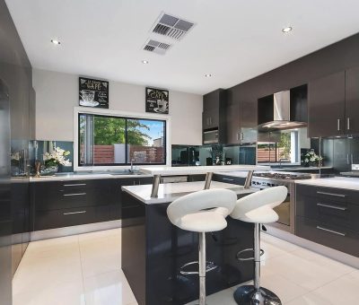 Modern kitchen with glossy black cabinets, a central island with two white bar stools, stainless steel appliances, and a window view of greenery.
