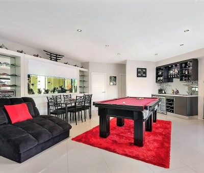 Stylish game room with a red pool table on a matching rug, black seating with red cushions, glass shelves, and a mini bar, creating a lively, modern vibe.
