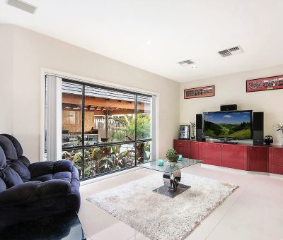 Modern living room with a black recliner, large window, red entertainment unit with a TV, glass coffee table on a white rug, and a serene atmosphere.