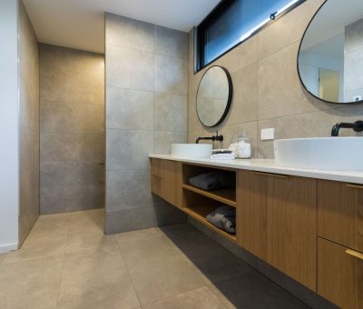 “Modern bathroom with floating wooden vanity, round mirrors, and walk-in shower.”